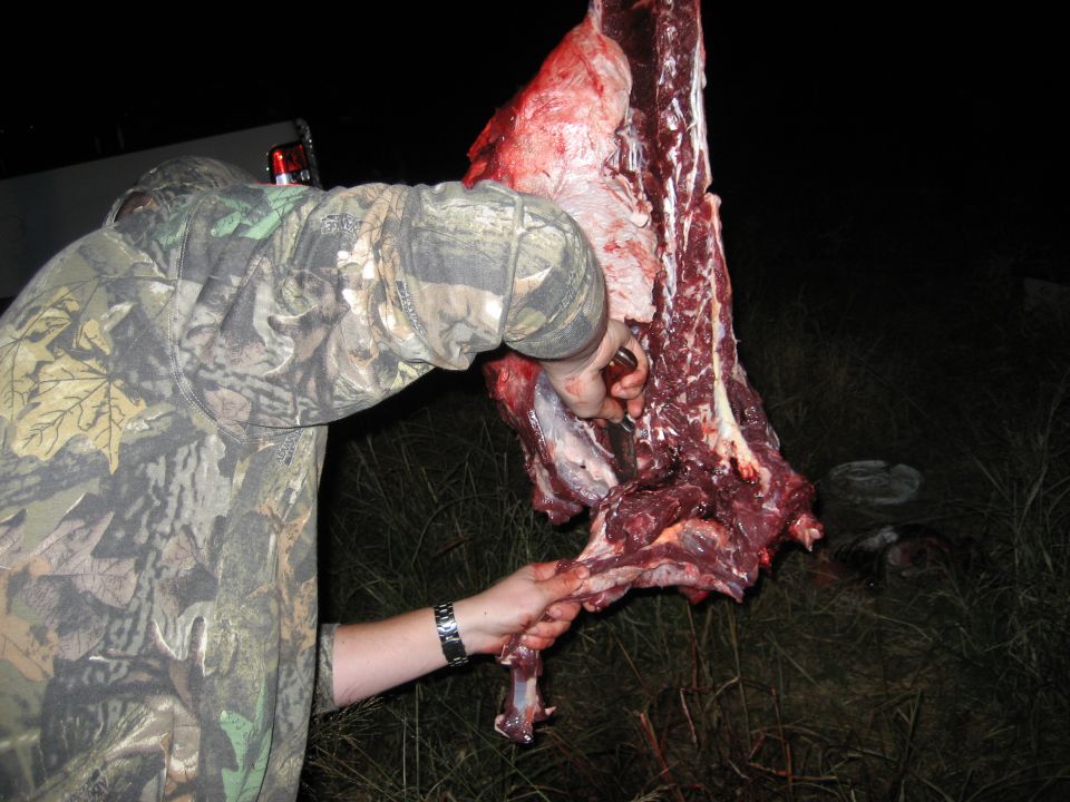 Person in camouflage butchering a large piece of meat outdoors at night