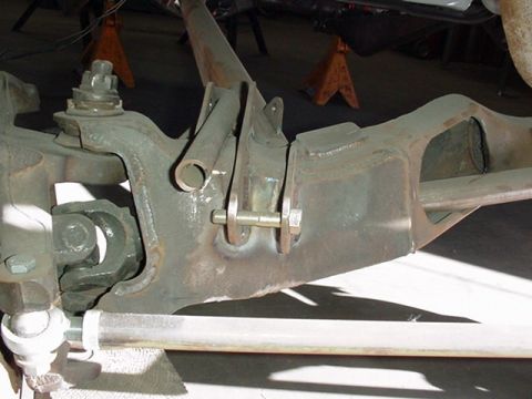1988 Ford Bronco - Close-up of a front suspension beam axle assembly painted olive-green, showing a large pivot bolt with washers, a mounting bracket, and a s…