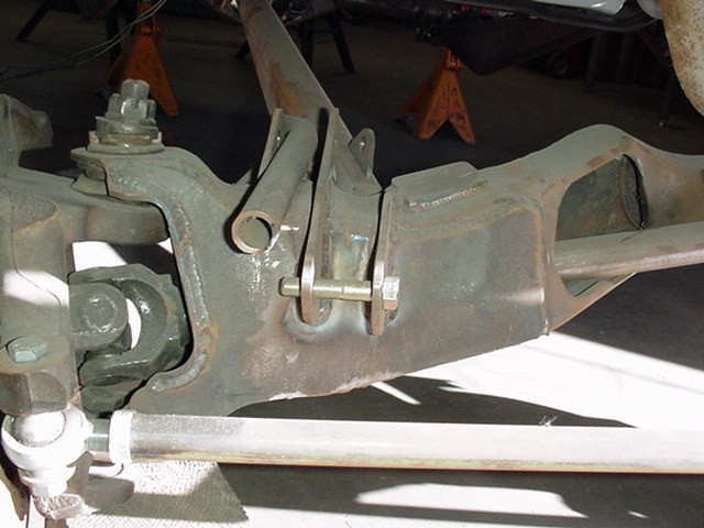 Green-painted front beam axle with pivot bolt and bracket, vehicle on jack stands