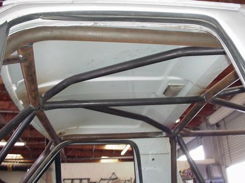 1988 Ford Bronco - Interior view looking up at the front roof area of a vehicle showing a welded tubular roll cage with unpainted bare-metal main hoop tube an…