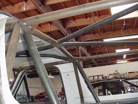 1988 Ford Bronco - Close-up of a bare-metal tubular roll cage under construction inside a vehicle, showing multiple welded intersecting bars and gusseted join…