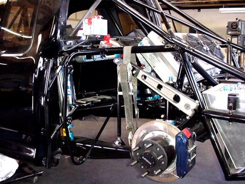1988 Ford Bronco - Close-up of a driver-side rear suspension and chassis on a stripped, tube-framed vehicle build, showing a vented brake rotor with hub, a bl…