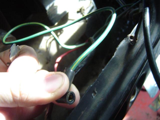 Hand holding a green and yellow wire connector near black metal structure