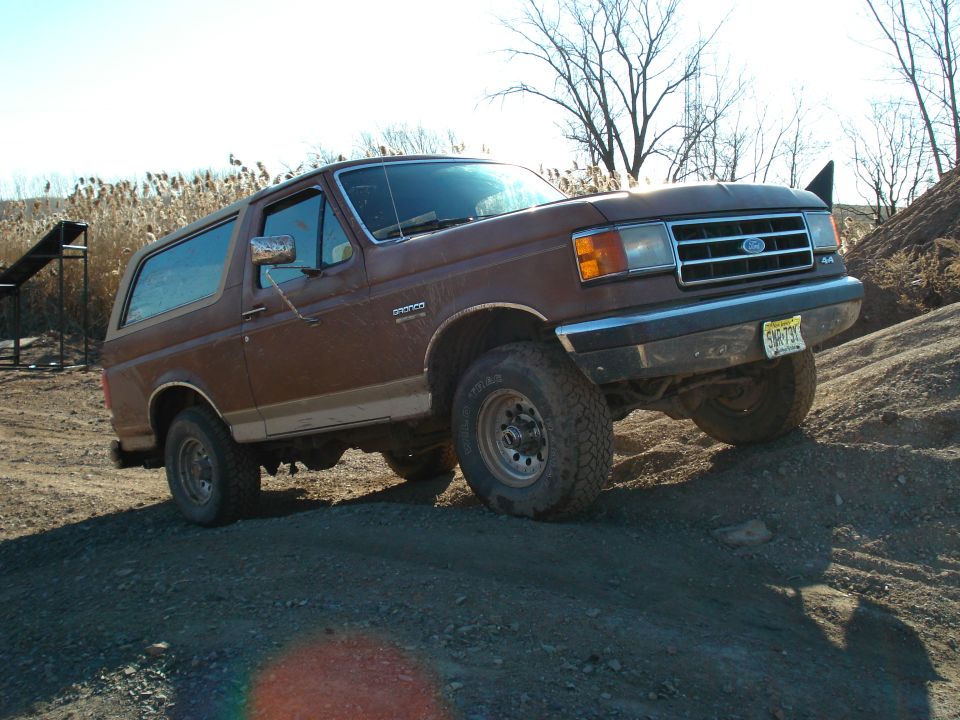 Brown 1987 Ford Bronco on dirt mound, front 3/4 view, showing grille and side panel