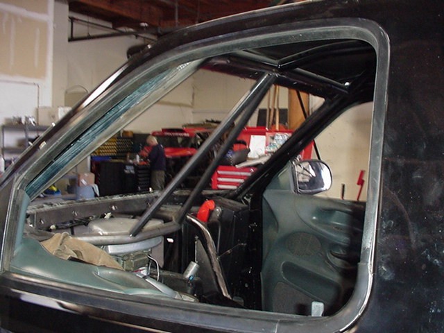 Roll cage inside stripped vehicle cab seen through door opening in a garage