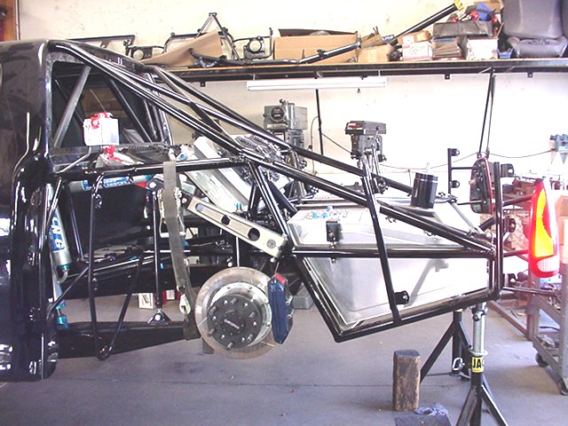 Tube-frame vehicle chassis with coilover, disc brake, and aluminum fuel cell in a garage