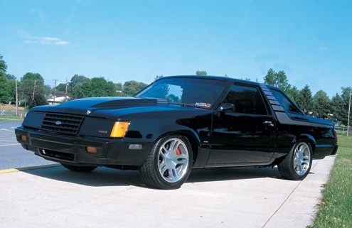 Lowered black Fox-body Ford coupe on polished wheels, front three-quarter view