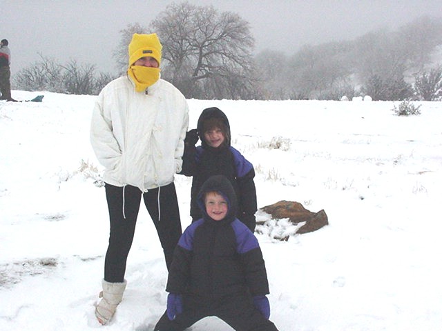 Adult and two children in winter clothing standing in a snowy field