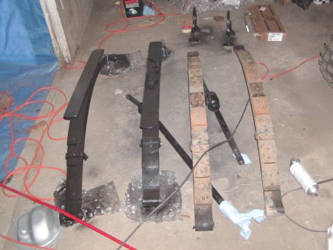 1991 Ford Bronco - Leaf springs and other suspension parts are laid out on the floor, possibly for repair or modification.