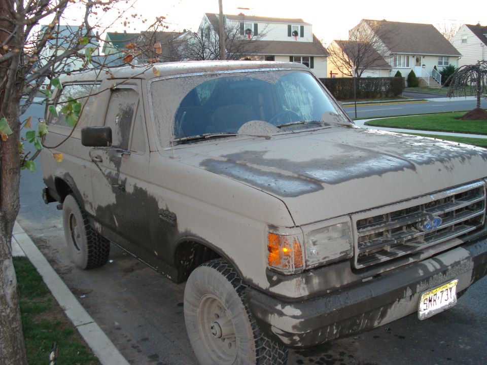 Mud-covered Ford Bronco parked on street. License plate is visible