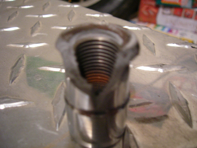 Close-up of a metal threaded part with orange interior, resting on a diamond plate surface
