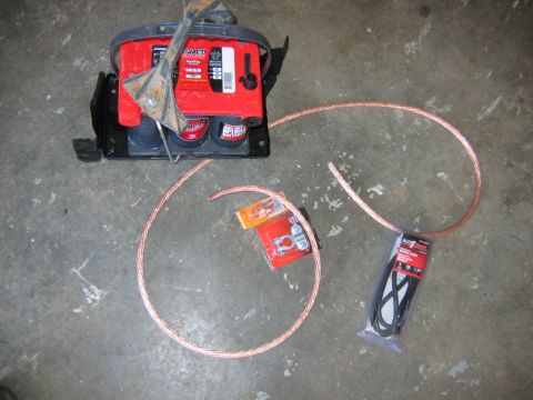 1992 Ford Mustang - A red Optima battery sits on a black mount next to coiled copper audio cables and a package of belts.