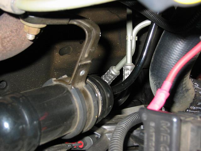 Under-hood close-up of black hose, metal lines with fittings, red wire, and a MEGA-labeled component