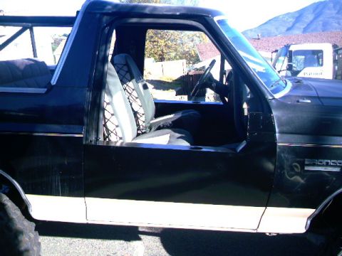 1989 Ford Bronco - The side profile of a black Ford Bronco shows its open driver's door and interior details.