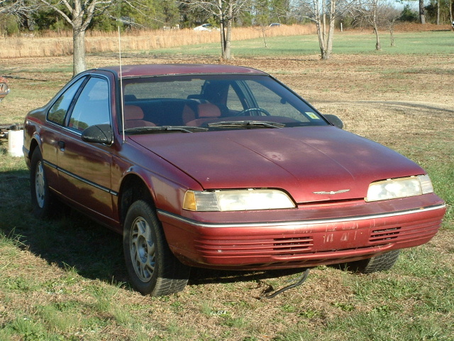 Red 1989 Ford Thunderbird coupe parked on grass, front 3/4 view