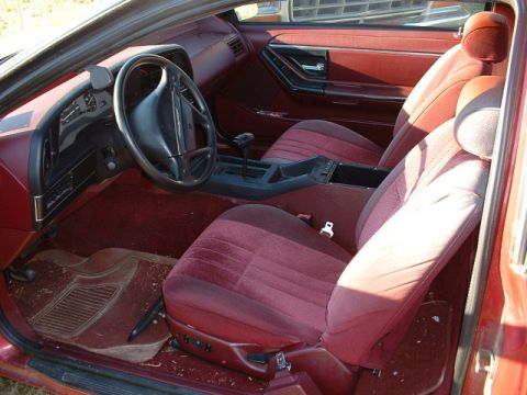 1989 Ford Thunderbird - The interior of this car features red velour seats and a dashboard with a prominent steering wheel.