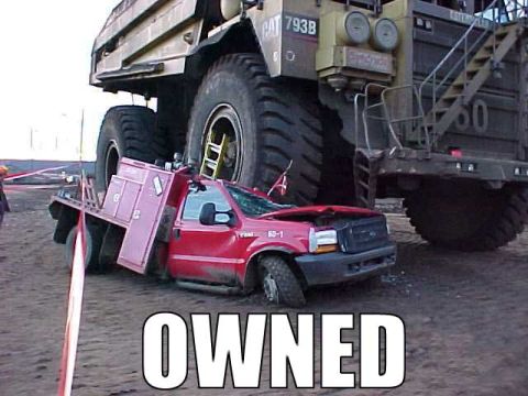 1995 Ford Bronco - A red pickup truck has been crushed by a colossal mining truck, illustrating a significant power imbalance.