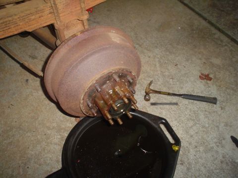 1967 Ford F-250 - A rusty rear axle hub and brake drum assembly from a 1967 Ford F-250 is shown with a drain pan and tools nearby.