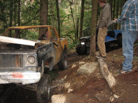 1990 Ford Bronco - Two off-road vehicles are stuck in a wooded area, with people attempting to free them.