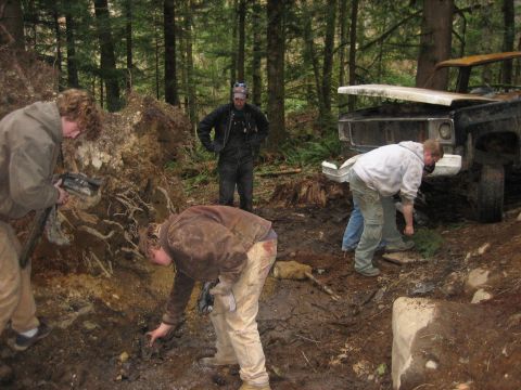 1990 Ford Bronco - Several people are gathered around a muddy, off-road vehicle that appears to be stuck in the woods.