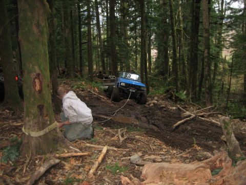 1990 Ford Bronco - Off-road vehicles navigate a challenging muddy terrain in a dense forest environment.