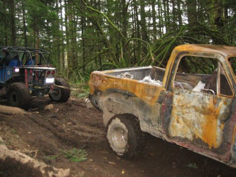 1990 Ford Bronco - Two vehicles are seen on a muddy forest trail, one a heavily damaged pickup truck and the other an off-road buggy.