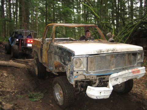 1990 Ford Bronco - A heavily damaged pickup truck navigates a muddy forest trail, followed by another off-road vehicle.