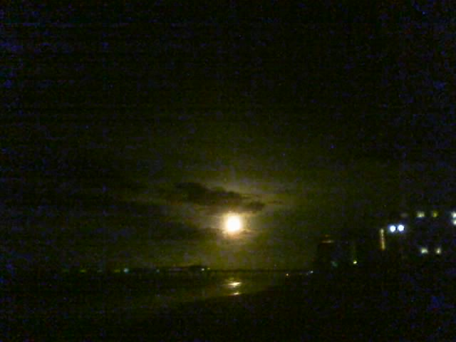 Night scene with moon, clouds, and distant lights reflecting on water