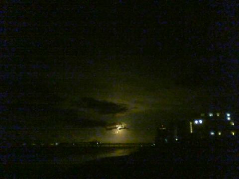 1989 Ford Bronco - A nighttime scene shows the moon partially obscured by clouds over a body of water, with illuminated buildings in the distance.