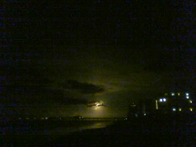 Moonlit sky over water with distant building lights