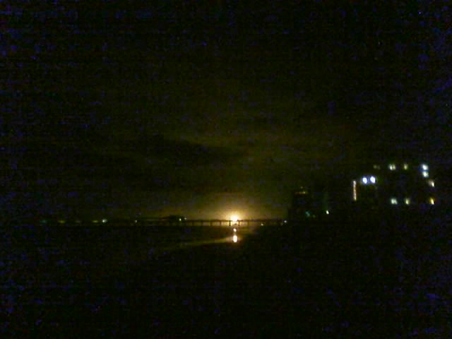 Distant industrial buildings and a bridge at night, illuminated by a bright light source
