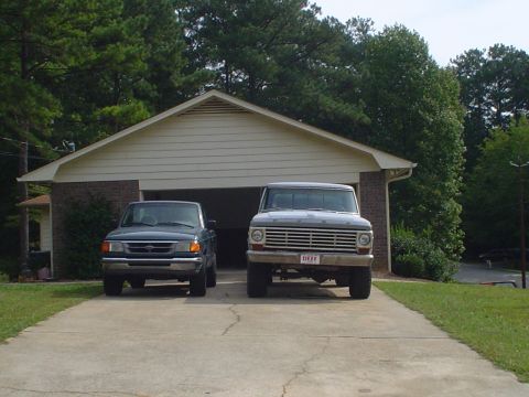 1967 Ford F-250 - A 1967 Ford F-250 and a dark green pickup truck are parked in a driveway in front of a garage.