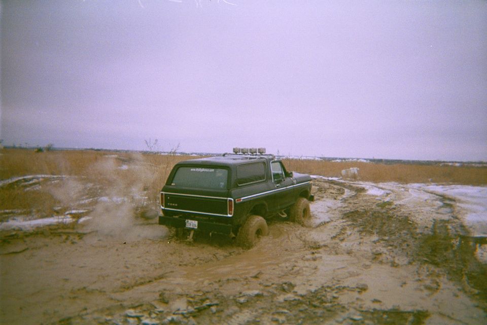Black Ford Bronco throwing mud as it powers through a frozen field, rear view