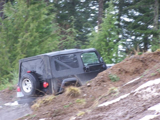 Black soft-top SUV climbing a steep muddy off-road hill, rear view