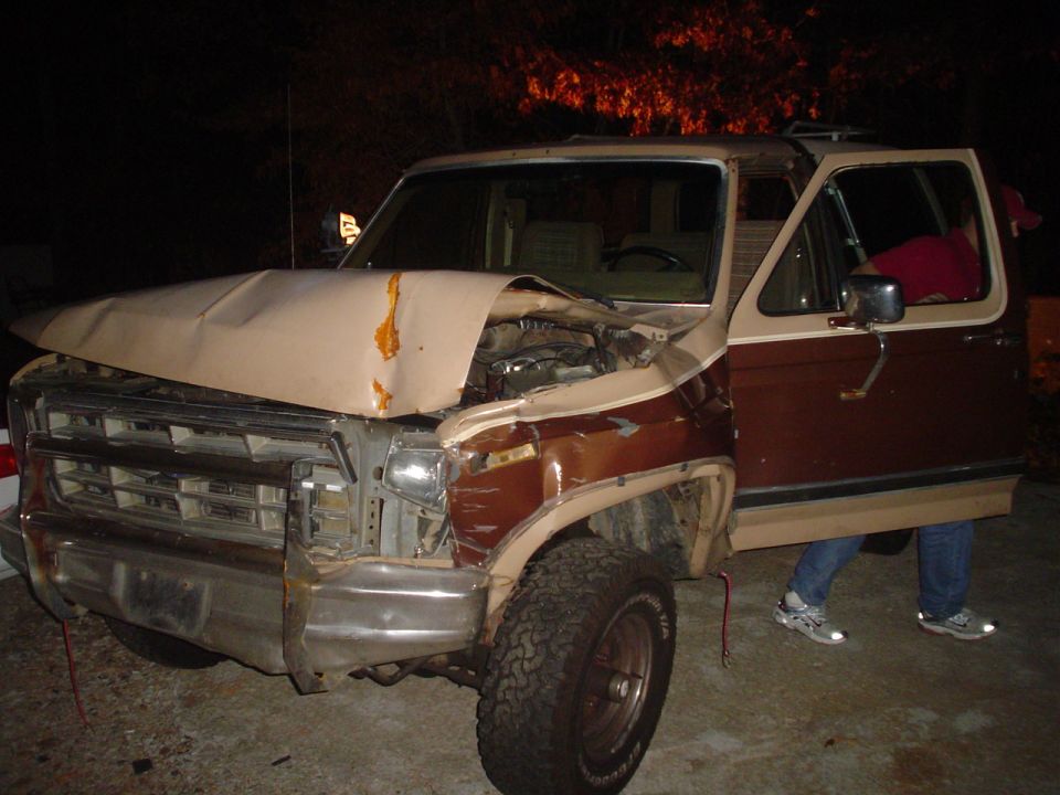Damaged brown and tan 1980s SUV with crumpled hood and open driver's door