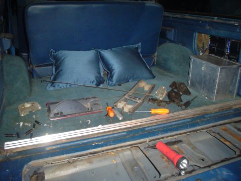 1984 Ford Bronco - Tools and disassembled parts are laid out in the cargo area of a vehicle, possibly during a repair or modification.