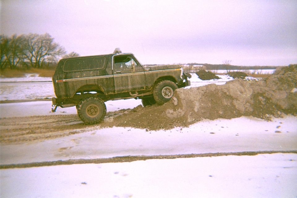 Dark Ford Bronco climbing a dirt berm on a snowy frozen lakeshore