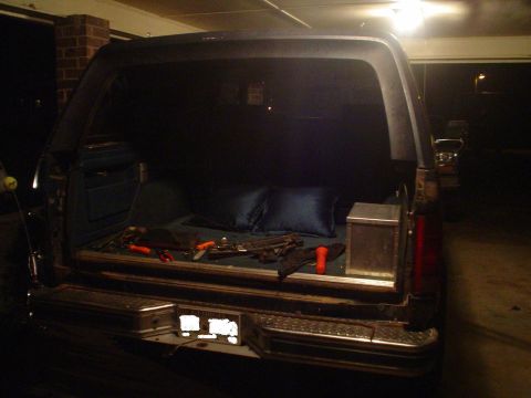 1984 Ford Bronco - Open tailgate of an SUV showing tools and pillows in the cargo area, parked in a garage.