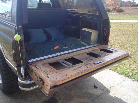 1984 Ford Bronco - The open tailgate of a Ford Bronco reveals a cargo area with pillows and tools, suggesting repair work.