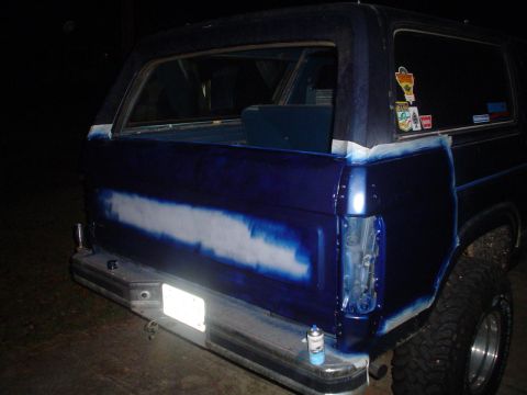 1984 Ford Bronco - The rear of an SUV is being prepped for paint, with masking tape applied to protect areas not being worked on.