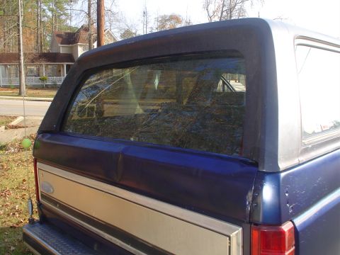 1984 Ford Bronco - The rear of a blue and tan 1984 Ford Bronco shows a dented tailgate.