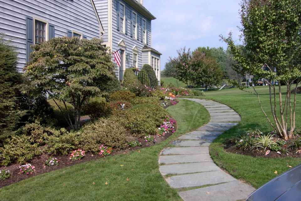 Colonial house with flagstone path and landscaped garden; car edge at lower right