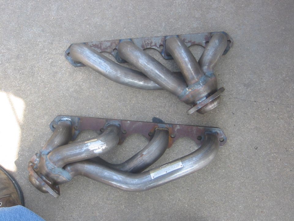 Pair of metal exhaust headers lying on a concrete floor