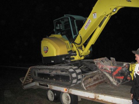 1974 Ford F-100 - Excavator loaded onto a trailer at night, with a person observing.