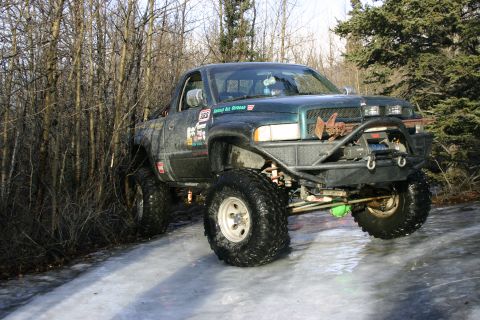 2003 Jeep TJ - A heavily modified pickup truck navigates an icy path through a wooded area.