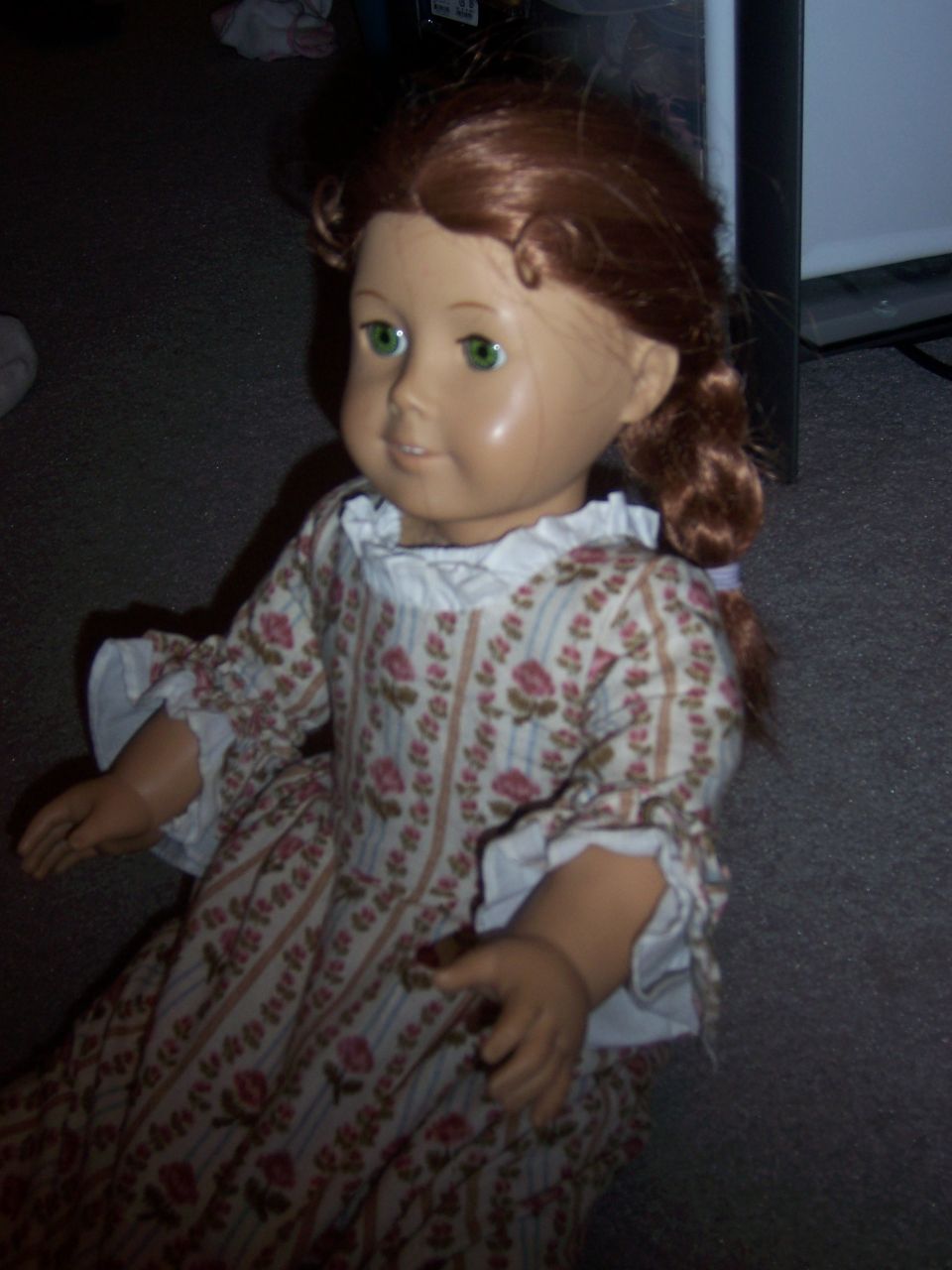 Doll in a floral dress with braided hair and green eyes, sitting on carpet
