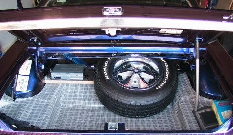 1968 Mercury Cougar - The trunk of a car contains a spare tire, an amplifier, and a plaid liner, with a watermark visible at the bottom.