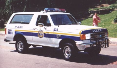 1986 Ford Bronco - This police SUV, likely a 1987 model, features distinctive markings including "POLICE" and "DIAL 911" on its exterior.