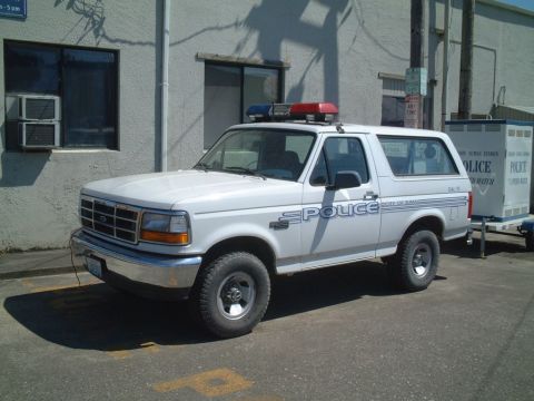 1986 Ford Bronco - This white Ford Bronco police SUV, likely from the early to mid-1990s, is equipped with a light bar and "POLICE" markings.