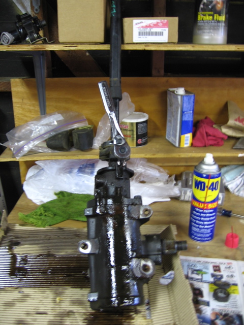 1989 Ford Bronco - A greasy power steering gearbox is shown on a workbench, with tools and cleaning supplies nearby.